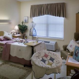 A cozy bedroom with a bed, rocking chair, and window letting in daylight.