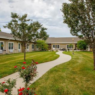 A peaceful garden with a walkway leading to a building surrounded by trees and well-maintained grass.