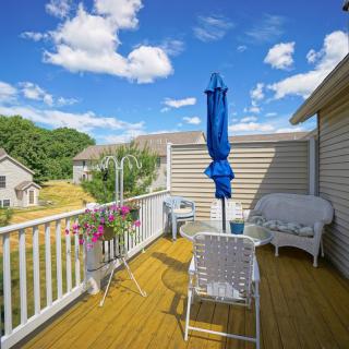 A sunny deck with outdoor seating, including a blue umbrella, chairs, and a small table with flowers.