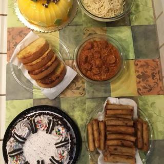 An assortment of dishes including cakes, noodles, and spring rolls arranged on a table.
