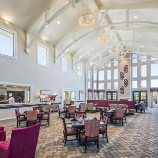 A spacious and elegantly designed dining area with high ceilings and large windows, featuring comfortable seating arrangements.