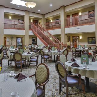 A spacious dining area with elegantly set tables and a grand staircase in the background.