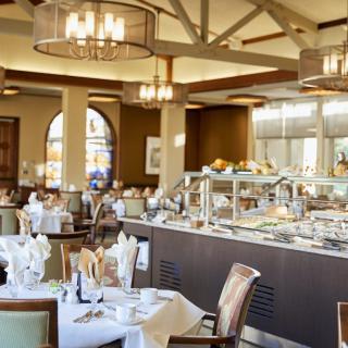 An elegant restaurant interior featuring a buffet setup, with neatly arranged tables and chairs under stylish chandeliers.