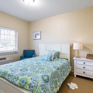 A cozy bedroom with a patterned bedspread, nightstand, and blue armchair.