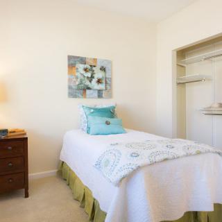 A cozy bedroom with a single bed, decorative pillows, and an open closet.