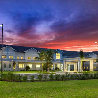 A beautifully lit building sits against a vibrant sunset sky with a well-maintained lawn in the foreground.