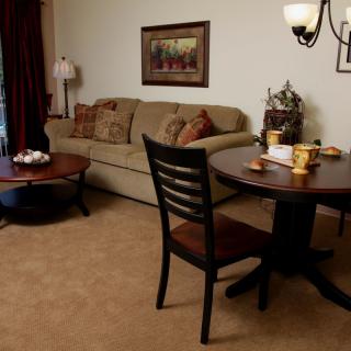 A cozy living room with a sofa, round wooden tables, chairs, and warm lighting.