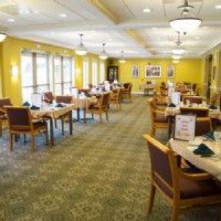 An empty dining room with neatly arranged tables and chairs, featuring large windows and warm lighting.