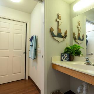 A bathroom featuring a sink with a decorative anchor mirror, potted plant, and towels.