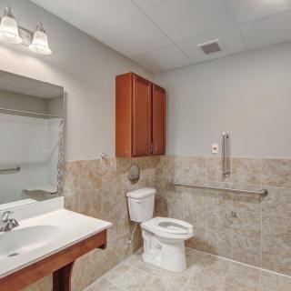 A modern bathroom with a sink, toilet, and wooden cabinet, featuring tiled walls and floor.