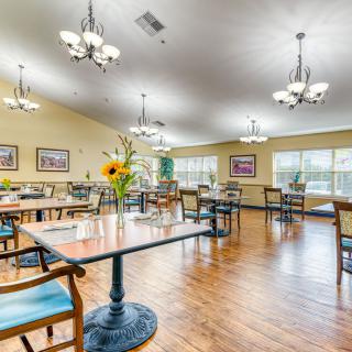 A well-lit dining area with arranged tables and chairs, decorated with flowers and paintings.