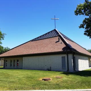 A modern church building with a cross on top, surrounded by green grass.
