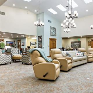 A spacious and modern living room with comfortable recliner chairs, sofas, and elegant chandeliers.
