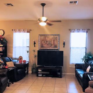 A cozy living room setting featuring dark leather couches, a television, and natural light from two windows.