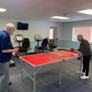 Two seniors playing table tennis in a recreation room.