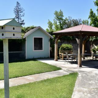 A sunny backyard with a gazebo and birdhouse, surrounded by a green lawn and trees.