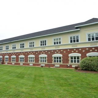 A two-story building with large windows and brickwork, surrounded by a well-maintained lawn.