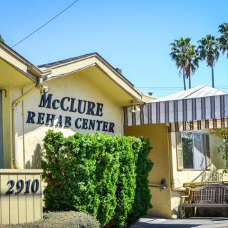 Exterior view of McClure Rehab Center with sign and surrounding greenery.