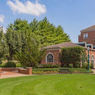 A brick building surrounded by lush trees and a well-maintained lawn on a sunny day.