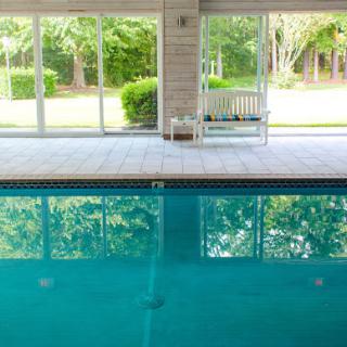 A serene indoor swimming pool bathed in natural light, surrounded by lush greenery.