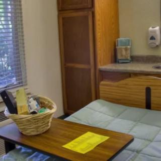 A hospital room with a bed, a wooden side table, and a basket on top.