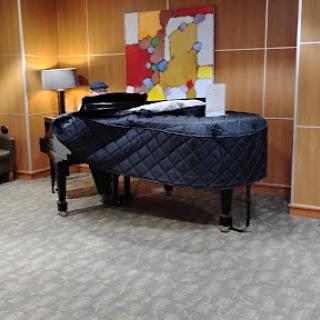 A grand piano covered with a protective quilt, set in a cozy interior space featuring modern artwork and a lamp.