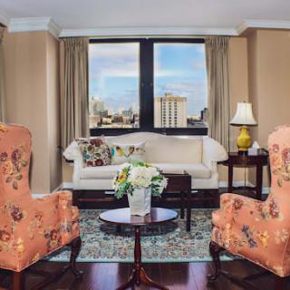 A well-furnished living room with a large window offering a city view, featuring a sofa, two armchairs, and a coffee table.