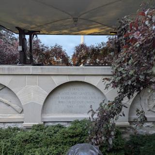 A serene monument surrounded by greenery and trees, partially sheltered under a canopy.