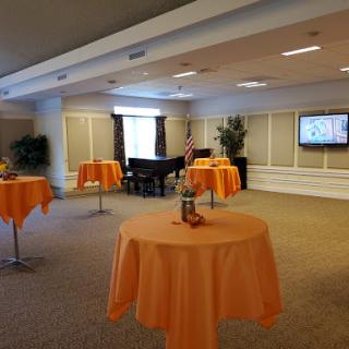 A spacious event room set up with orange tablecloths and a piano, ready for gatherings.