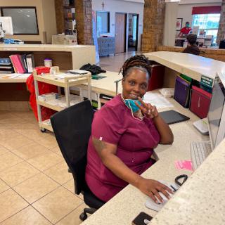 A friendly receptionist at her desk, smiling while working on her computer.