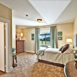 A cozy bedroom featuring a single bed, a dresser, and a large window with curtains.