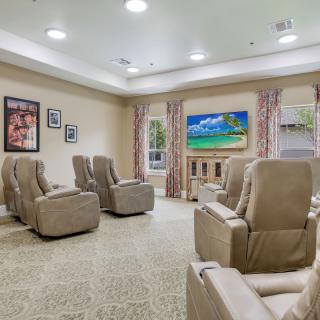 A cozy living room with recliner chairs facing a television, adorned with wall decor and curtains.