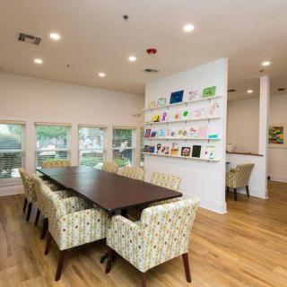 A modern meeting room with a large conference table surrounded by upholstered chairs, featuring wall-mounted artwork and natural lighting from multiple windows.