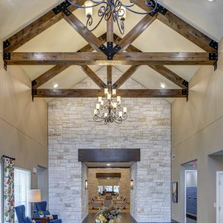 A spacious living room with a vaulted ceiling and exposed wooden beams, featuring a chandelier and a stone accent wall.