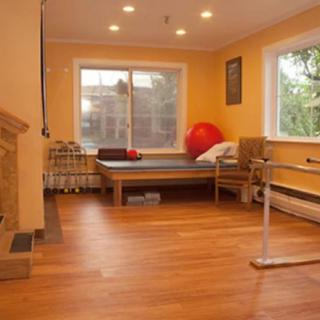 A warm and inviting exercise or therapy room with a ballet barre, wooden floors, and an exercise ball.