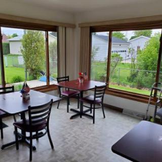 A small dining area with tables and chairs, featuring large windows offering a garden view.