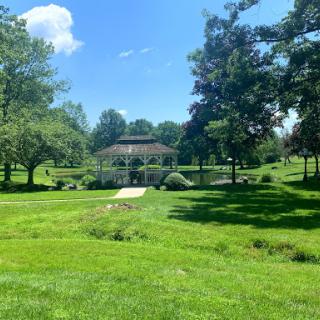 A serene park scene featuring a gazebo surrounded by lush greenery under a clear blue sky.