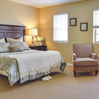 A cozy bedroom featuring a neatly made bed, an armchair, and warm lighting.