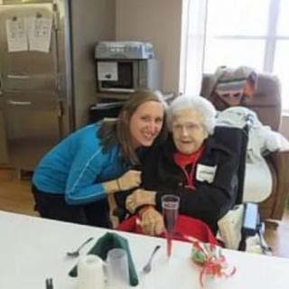 A young woman is hugging an elderly woman in a kitchen setting.