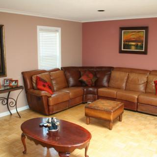 A cozy living room featuring a brown leather sectional sofa, wooden coffee table, and warm-toned walls adorned with artwork.
