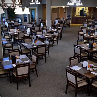 An empty dining room with neatly arranged tables and chairs, illuminated by chandeliers.