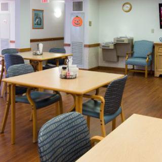 An empty dining area in a nursing home with tables and chairs arranged neatly.