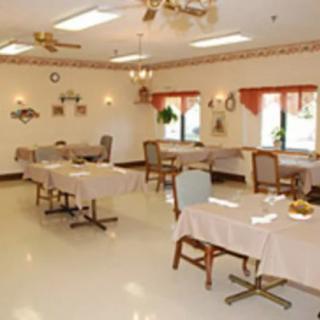 An empty dining room with neatly arranged tables and chairs, featuring windows, ceiling fans, and wall decorations.