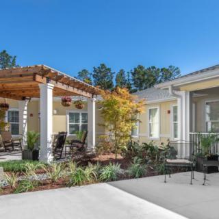 A charming residential patio with a pergola and outdoor seating, surrounded by well-maintained landscaping under a clear blue sky.