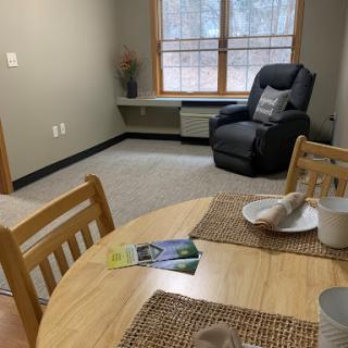 A cozy living and dining space with a wooden table and a comfortable chair by the window.