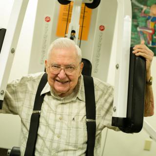 An elderly man smiling while using gym equipment.