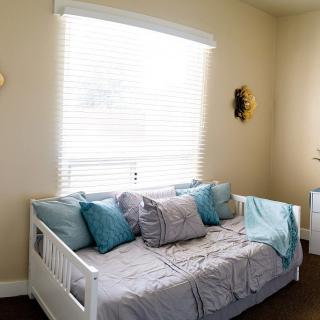A cozy bedroom featuring a daybed with blue and gray pillows, illuminated by natural light from a window.