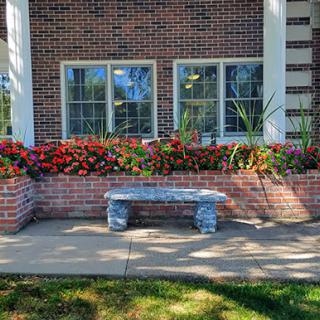 A serene spot with a stone bench surrounded by colorful flowers and a charming brick wall.