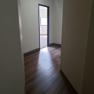 A hallway with a wooden floor leads to an open doorway revealing another room.