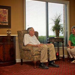 Two seniors are sitting in a cozy living room, engaged in conversation.
